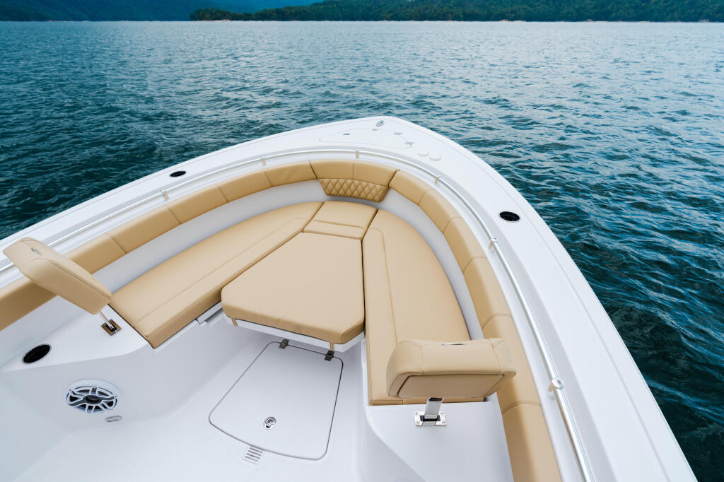 Boat's forward seating area with tan cushioned wraparound seats and white gelcoat hull overlooking calm blue water
