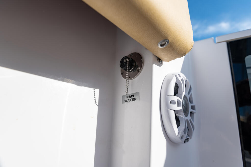 Raw water washdown outlet and white marine speaker mounted on boat cabin exterior under hardtop