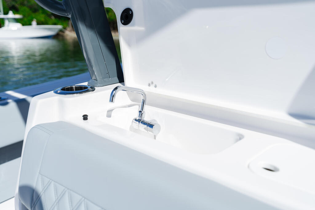 Chrome faucet and white sink basin on boat's starboard side with water and green shoreline visible