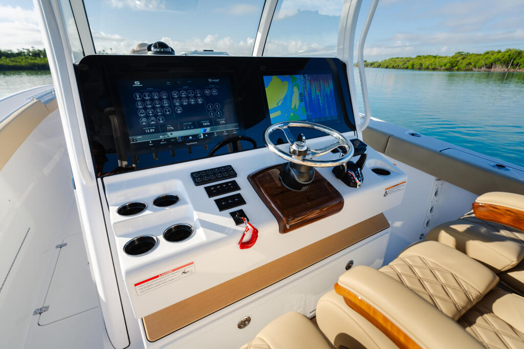 Helm station with dual touchscreen displays, steering wheel, and control panels overlooking calm coastal waters