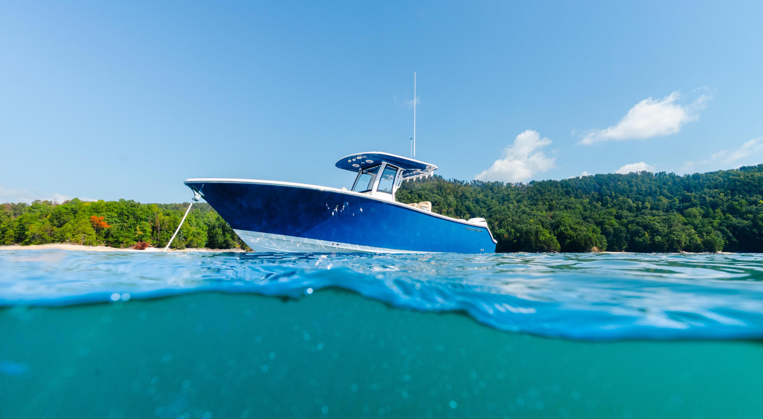 Blue fishing boat anchored in clear turquoise water with forested shoreline and sandy beach in background