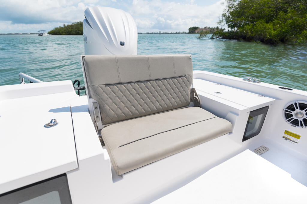 Rear fold-up bench seat with quilted gray upholstery and white engine mounted on a bay boat near mangroves