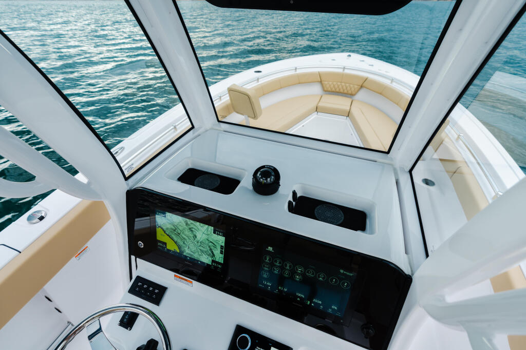 Helm station with GPS display, compass, and steering wheel overlooking cream-colored seating and open water