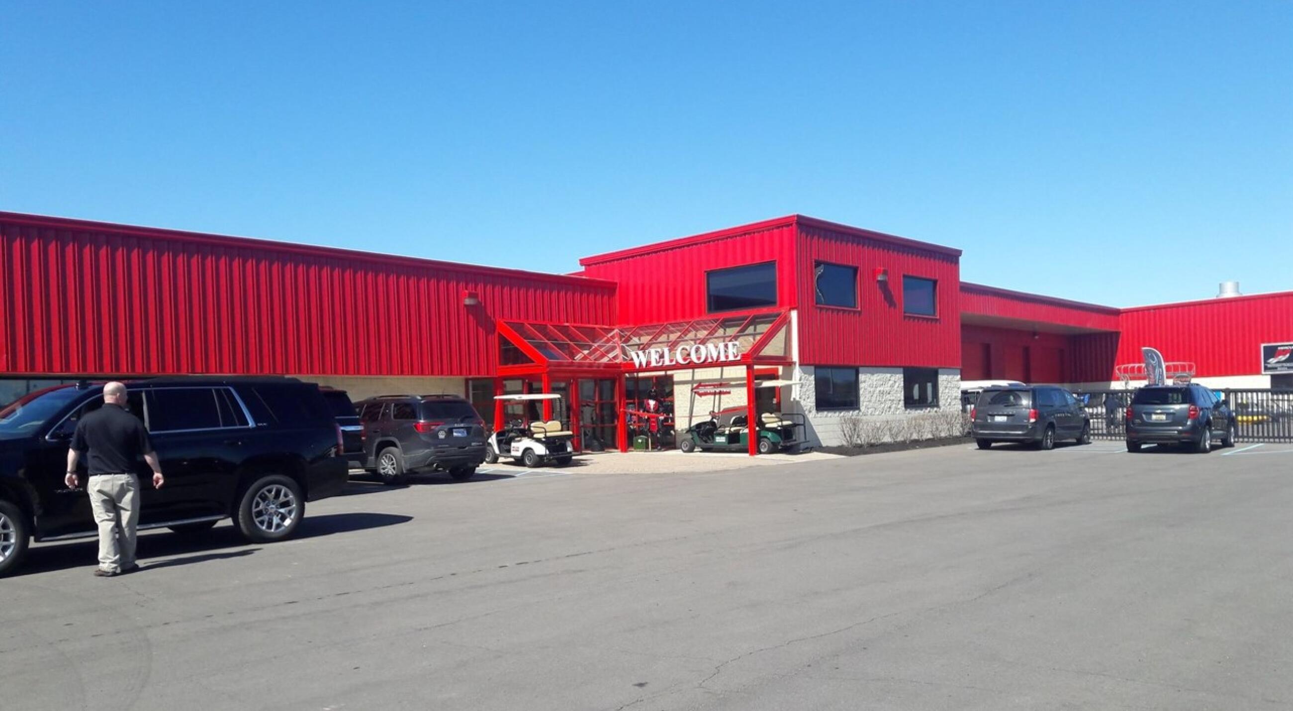 Bright red marine dealership storefront with welcome sign and parked vehicles under clear blue sky