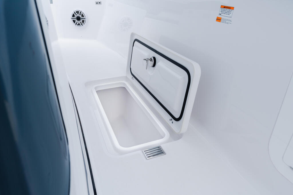 Open livewell compartment with drain plug on white fiberglass boat deck