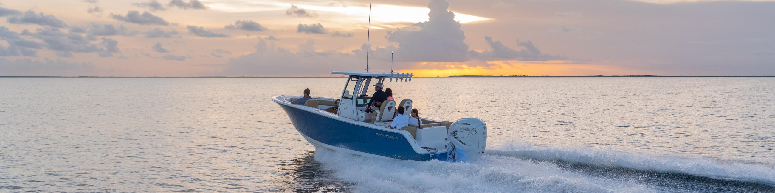 Blue and white center console boat running through shallow water at sunset near a sandy beach