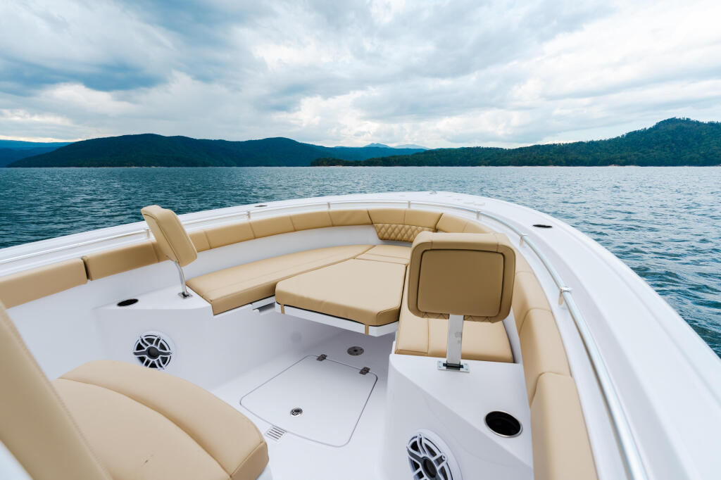 Spacious white boat with tan seating and console overlooking forested mountains and calm lake water