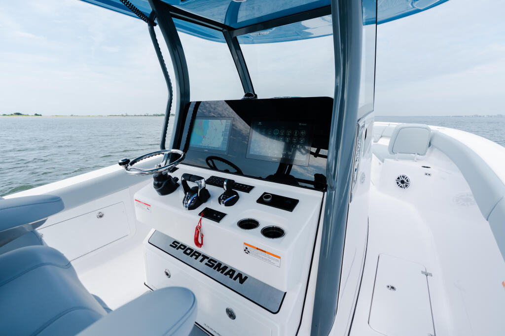 Helm station of Sportsman boat with hardtop, displaying GPS display, wheel, and control panel with open water in background