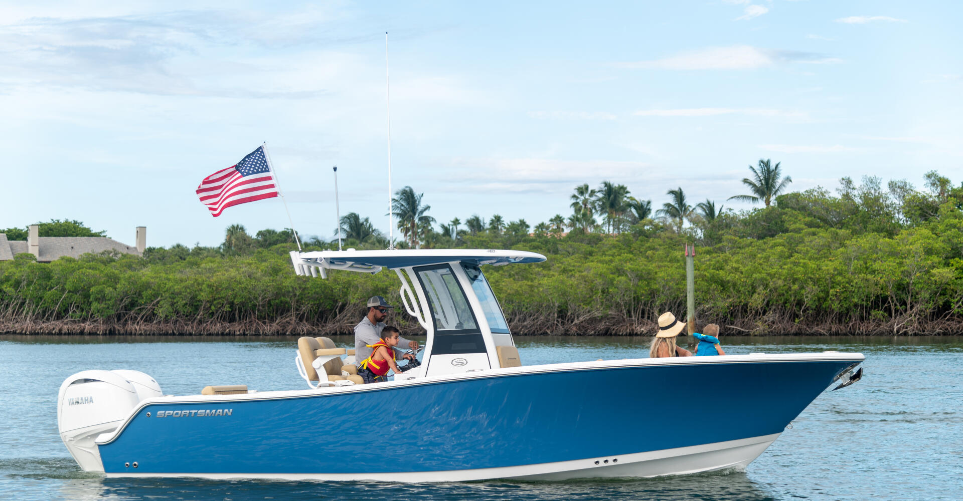 Family enjoying a blue center console boat in shallow coastal waters with mangroves and American flag visible