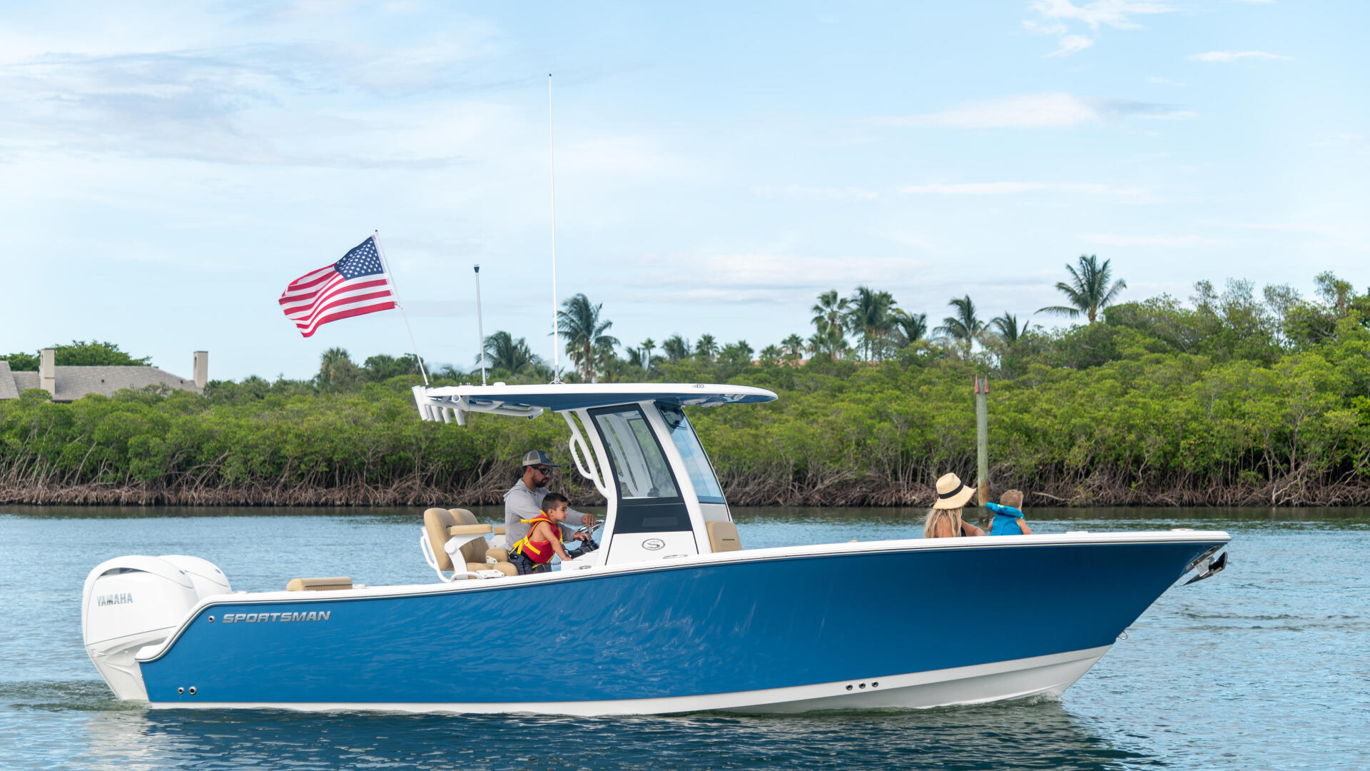 Family enjoying a blue center console boat in shallow coastal waters with mangroves and American flag visible
