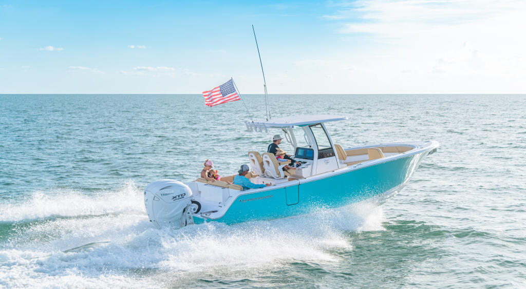 Turquoise center console boat with passengers cruising through shallow beach waters with American flag flying