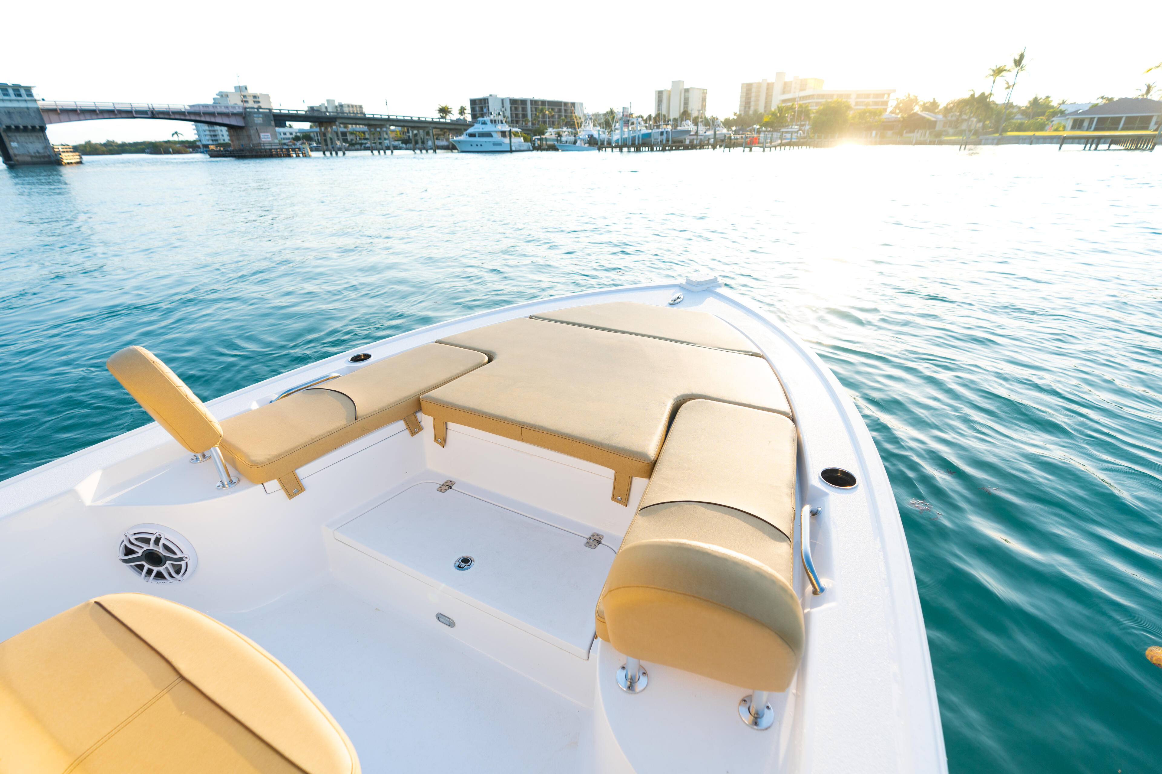Spacious open bow with tan seating and white fiberglass deck overlooking marina and coastal cityscape at sunset