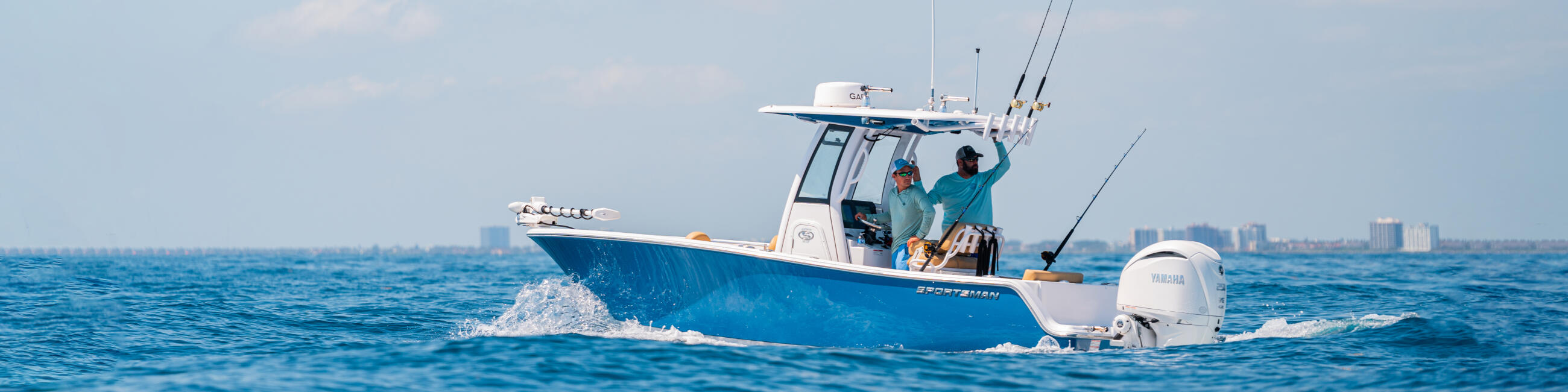 Two anglers in a blue center console boat fishing offshore with coastal skyline in the distance