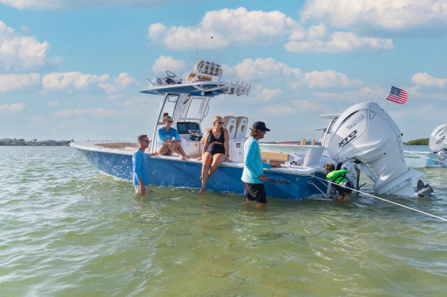 Family enjoying shallow water off a sandbar near a blue and white center console boat with hard-top