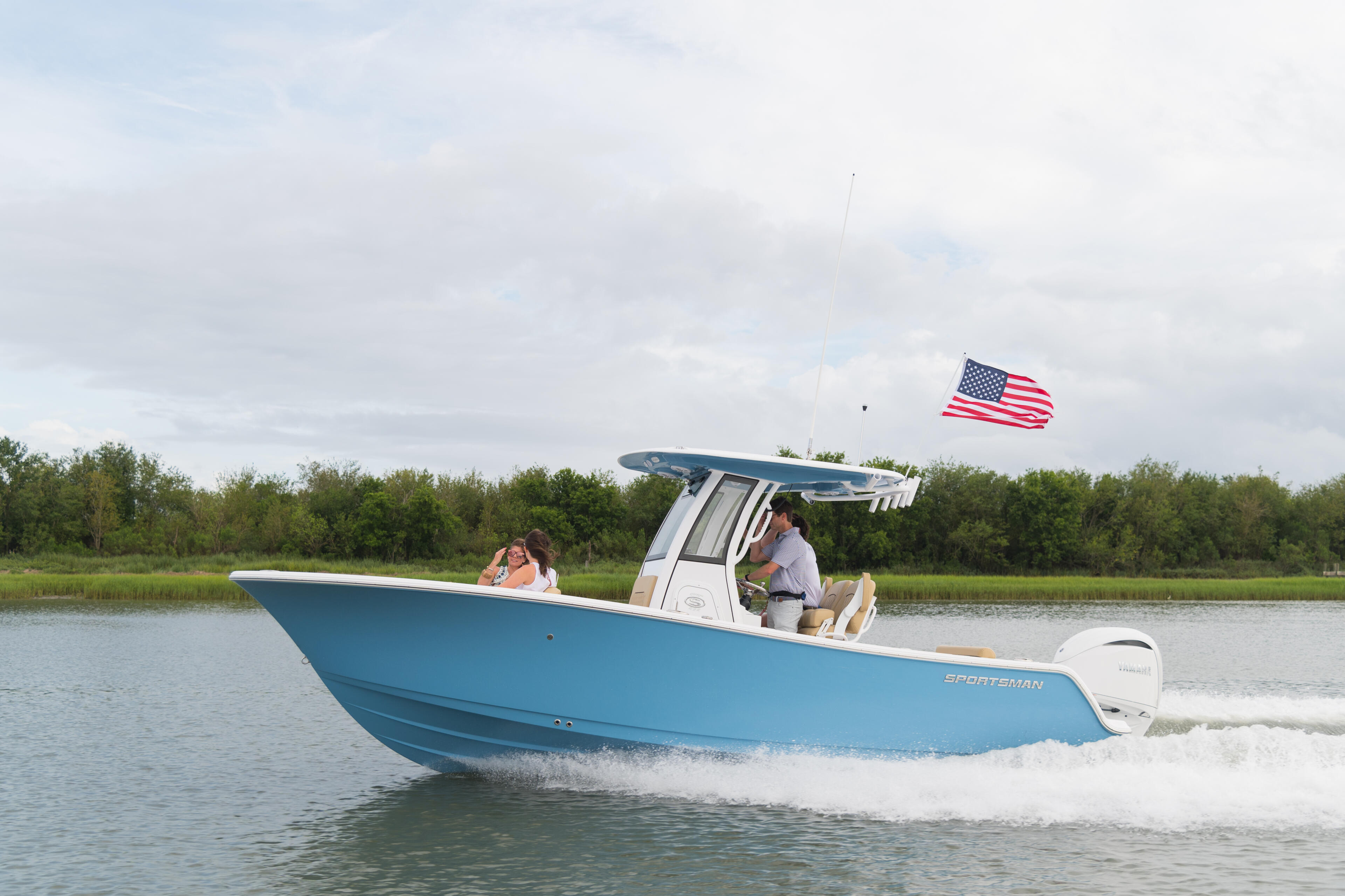 Blue sportsman boat running through shallow coastal water with two people aboard and American flag flying