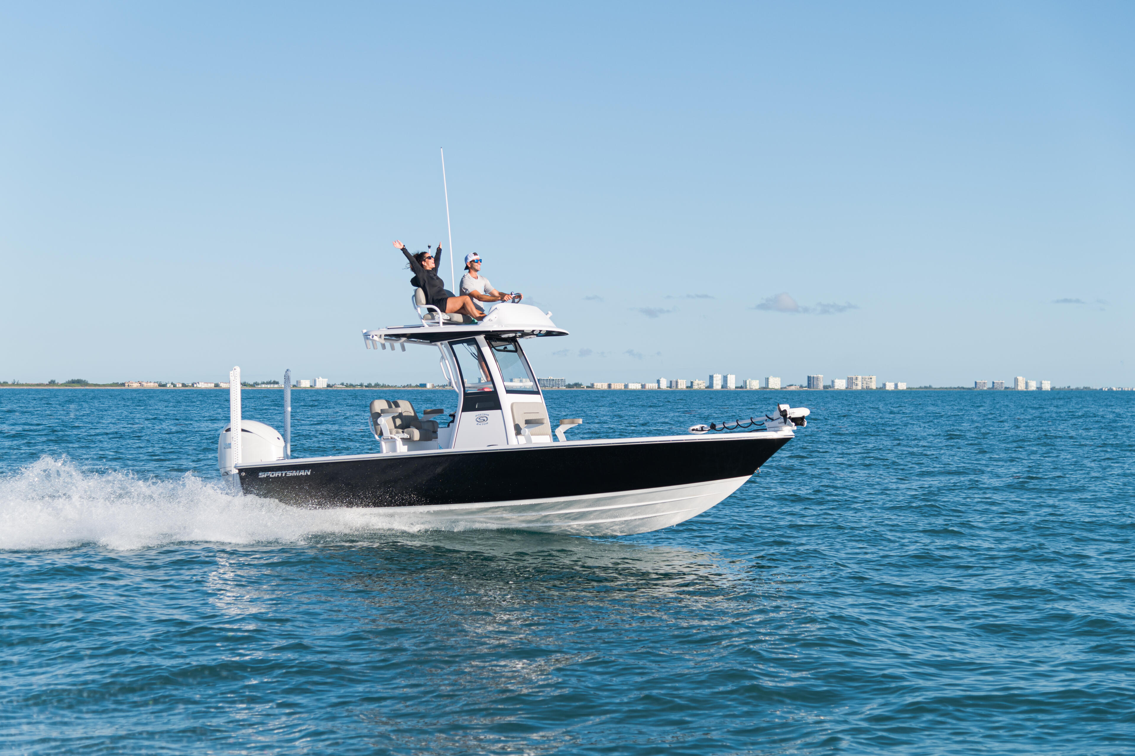 Center console fishing boat with two anglers on the tower running through shallow coastal waters near a beach