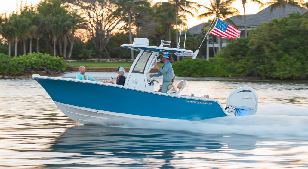 Blue and white center console boat running in shallow water with couple aboard near palm trees and waterfront homes at sunset