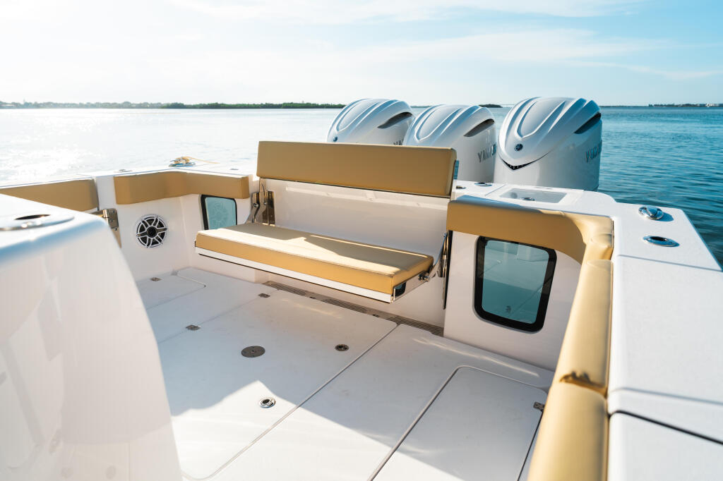 Spacious open cockpit with tan and white seating, three outboard engines, and calm blue water views