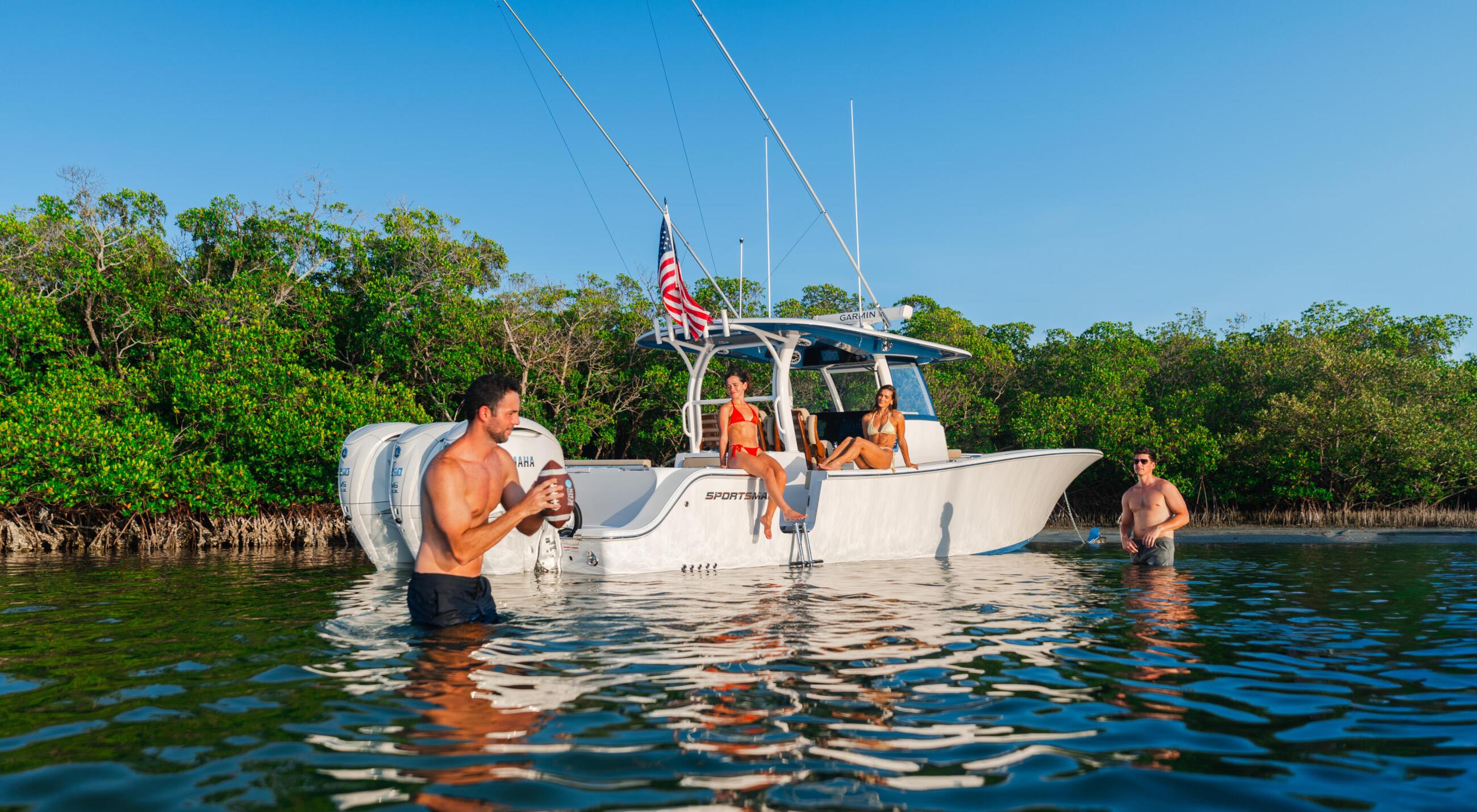 Group of friends swimming and relaxing around a moored sportfishing boat in shallow coastal waters