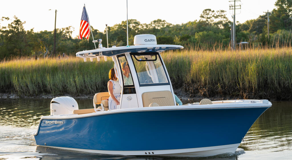 Blue center console boat anchored in calm marsh waters with American flag and hard-top canopy at sunset