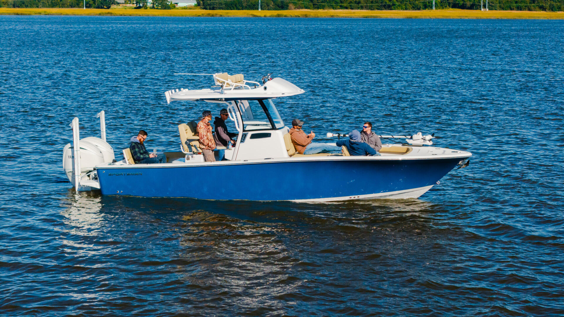 Blue and white center console boat with five people cruising on calm blue water near a sandy beach