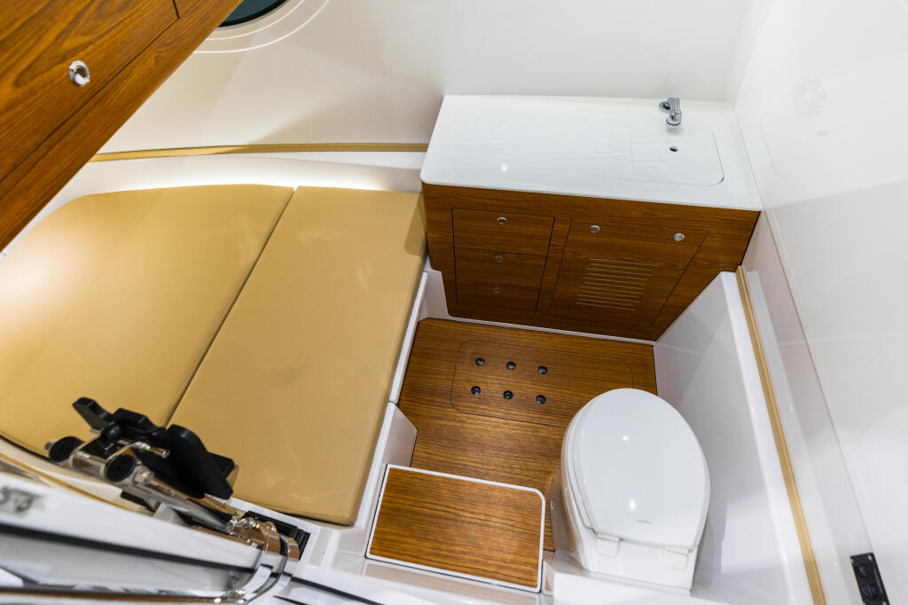 Boat cabin head with white toilet, pedestal sink, and wooden cabinetry with storage compartments