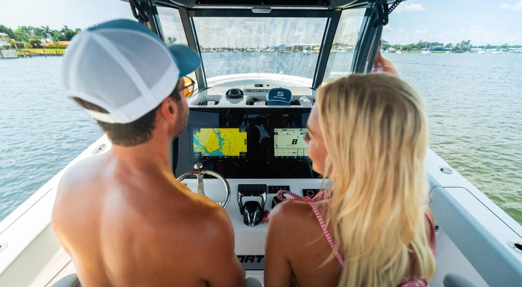 Couple at helm of center console boat with GPS and sonar displays overlooking marina