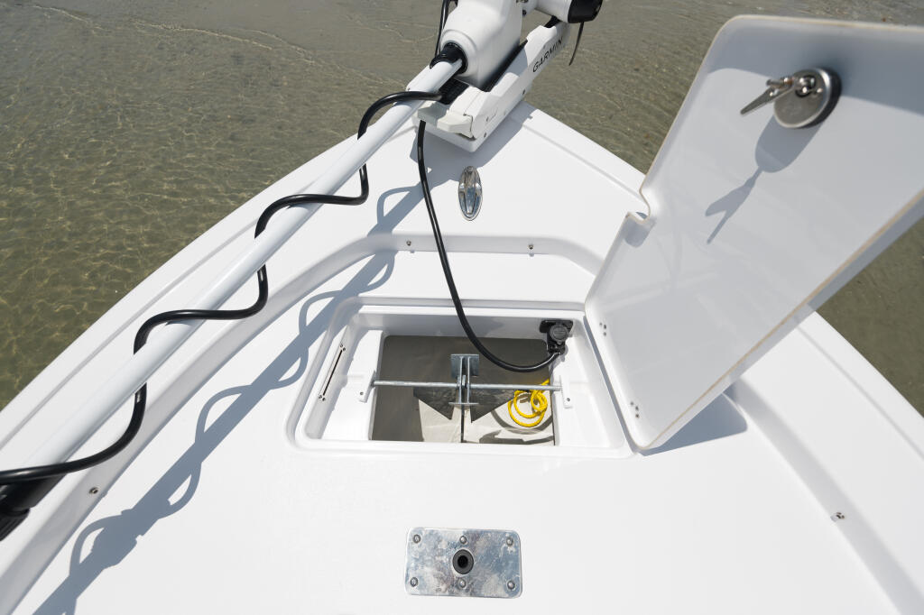 Boat bow deck with open anchor locker, rope storage, and electronics mounted on white gunwale over shallow water