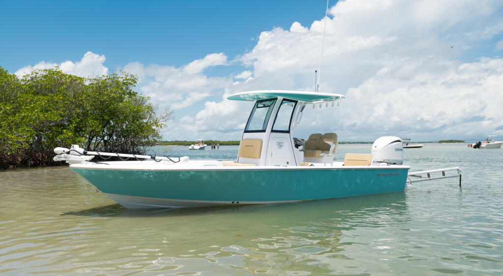 Turquoise and white bay boat anchored in shallow coastal waters near mangroves