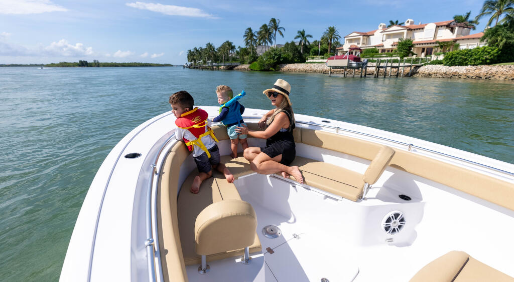 Woman and two young children cruising in an open center console boat near a waterfront home with palm trees