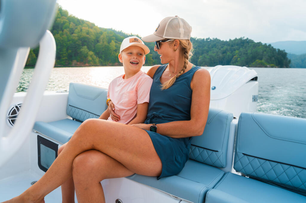Woman and young boy enjoy relaxed seating in the rear of a center console boat on a calm lake with forested shoreline