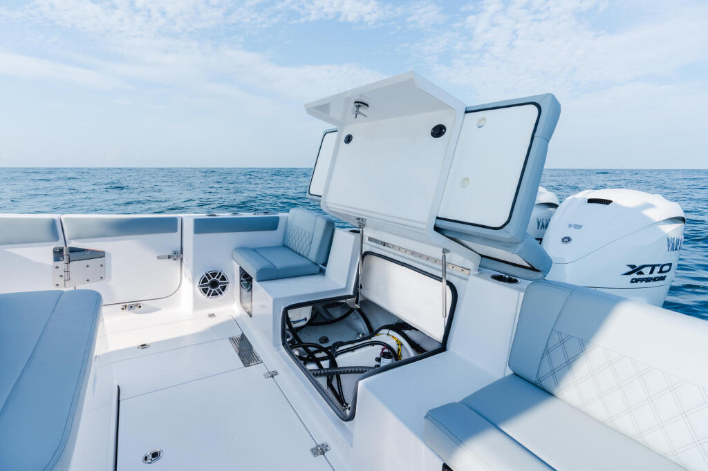 Open boat deck with blue and white seating, center console helm, and outboard motors on calm offshore water