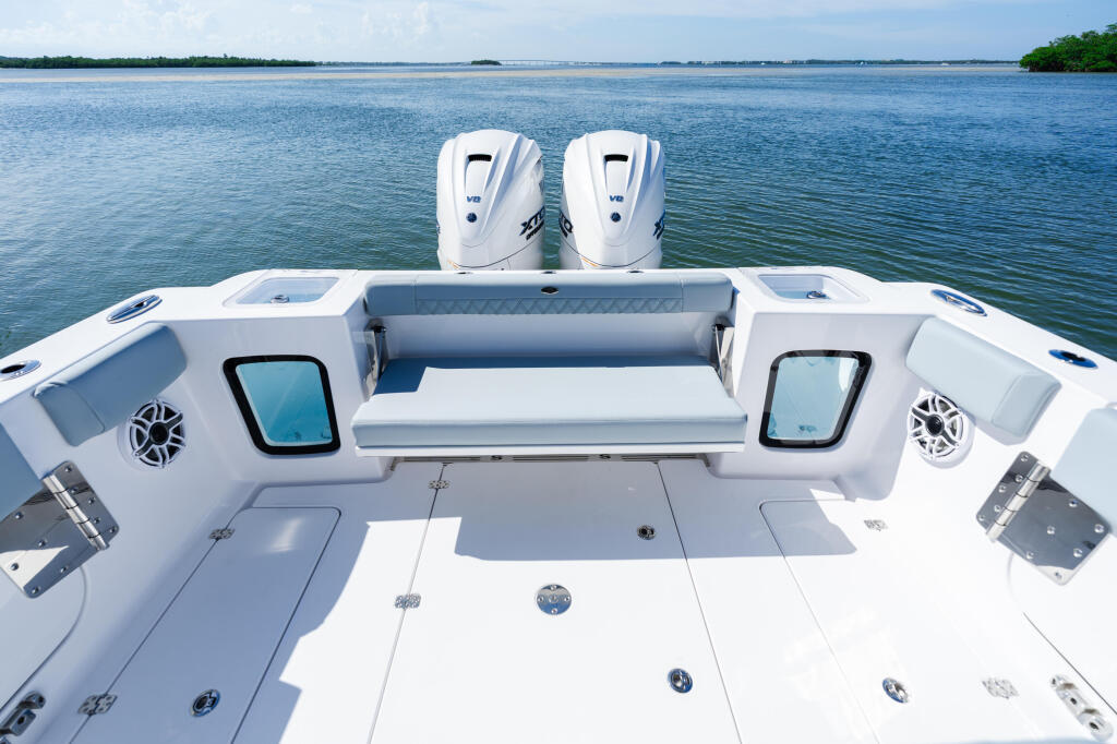 Overhead view of center console boat with dual outboard engines, cushioned seating, and open water shoreline behind