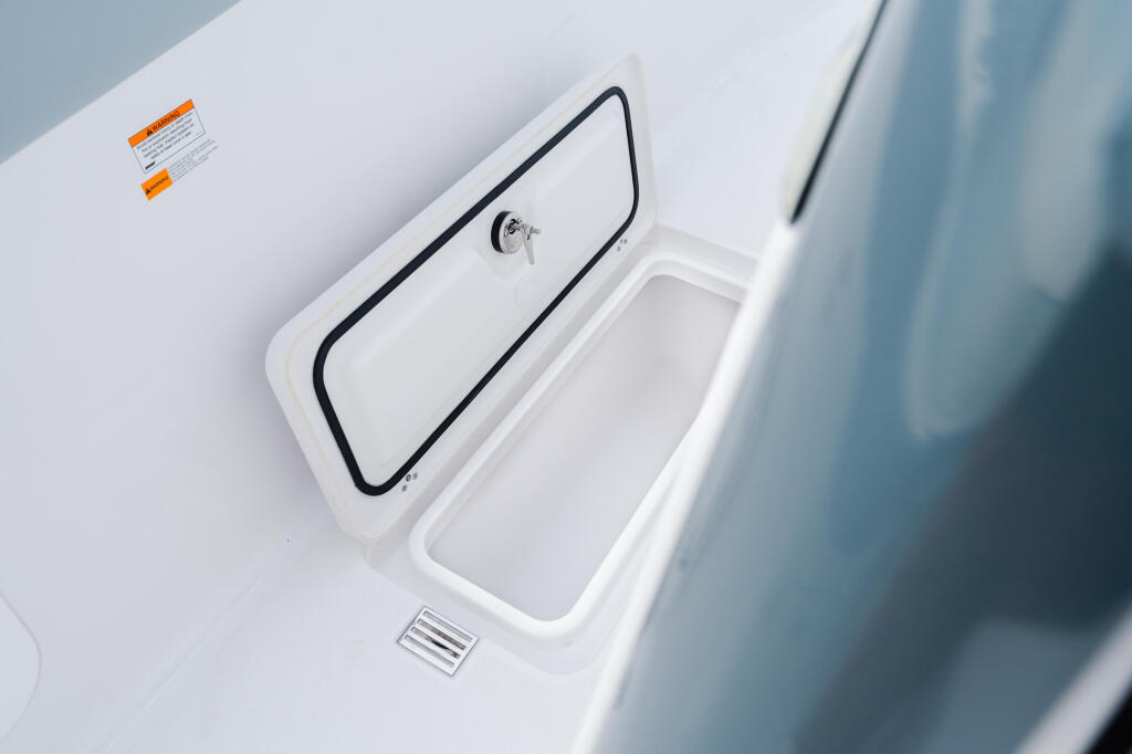 Open storage compartment on white boat deck with drain and manufacturer label visible