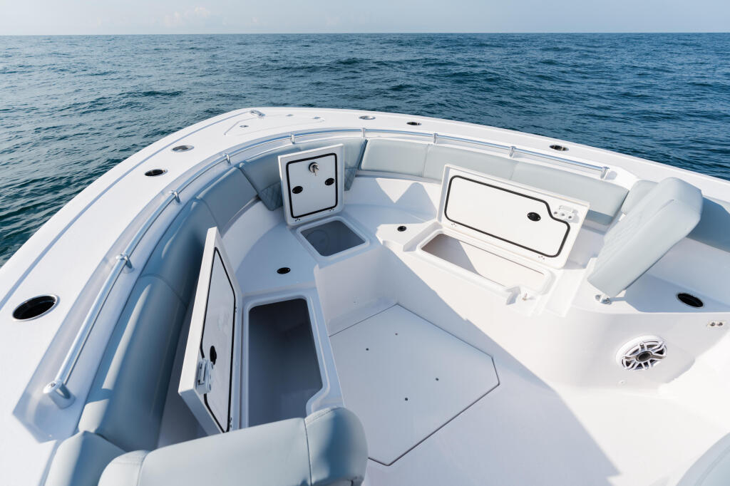 Spacious bow seating area of a white center console boat with multiple storage compartments on calm open water