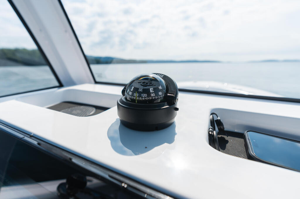 Compass mounted on white console with calm water and shoreline visible in background