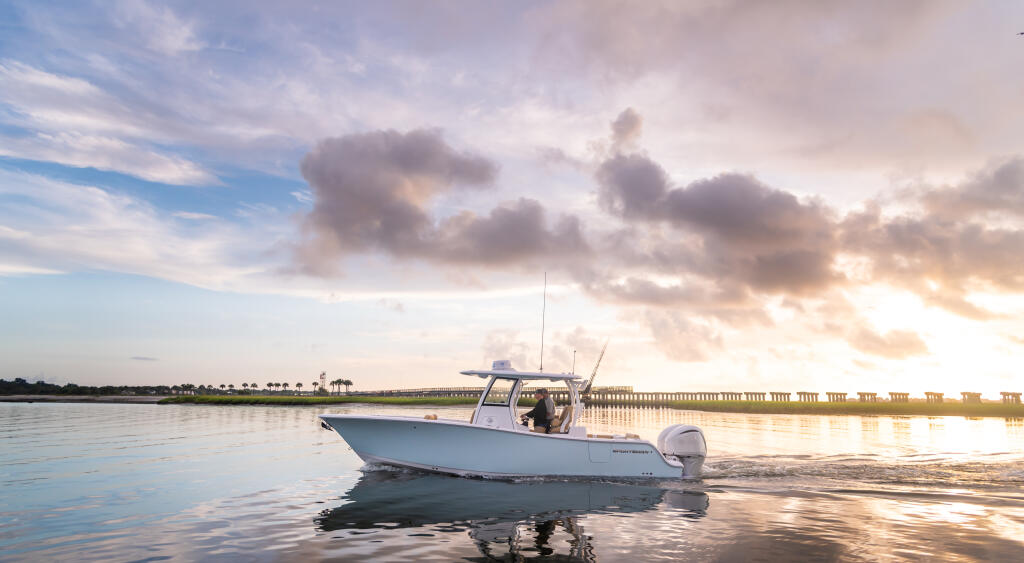 White center console boat anchored in shallow water at sunset with a long pier in the background