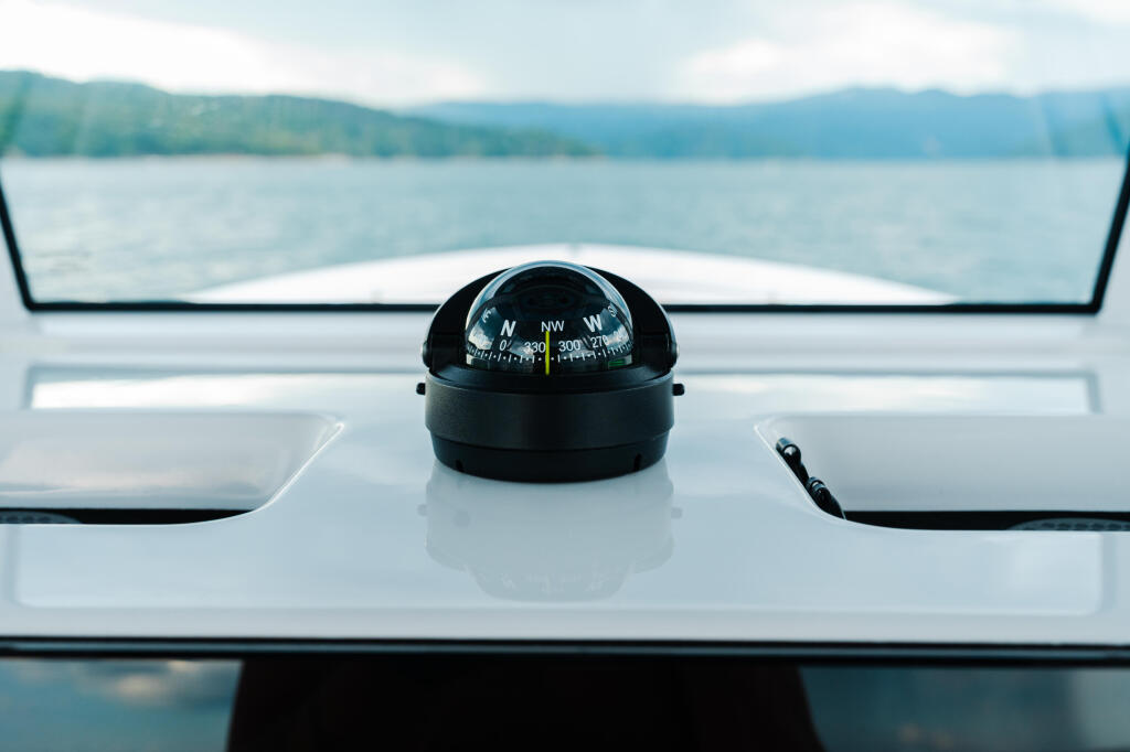 Compass mounted on boat helm dashboard with lake and mountains visible through windshield