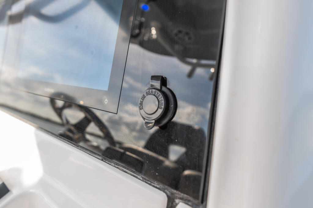 Close-up of a boat dash showing a black rotary knob control with sky reflection in the windshield