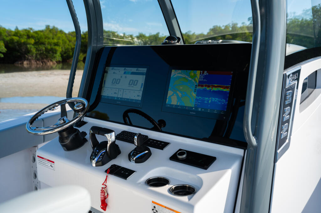 Helm station with dual touchscreen displays, steering wheel, and control panels overlooking shallow coastal waters and mangroves
