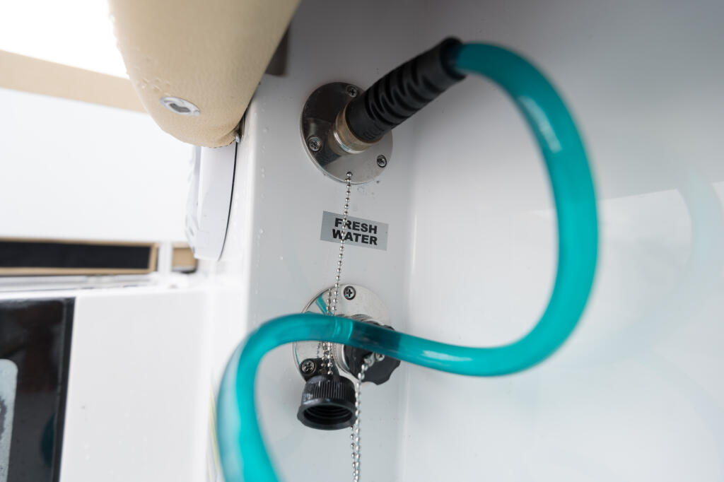 Fresh water washdown system with turquoise hose and labeled inlet mounted on cabin wall
