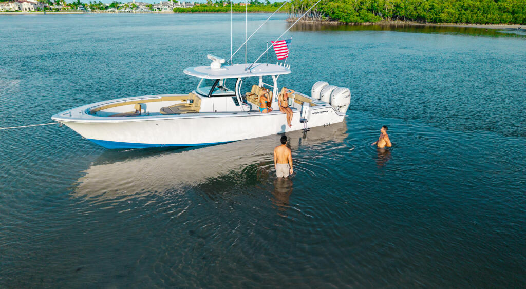 Couple swimming near a white center console boat anchored in shallow turquoise water at a sandbar
