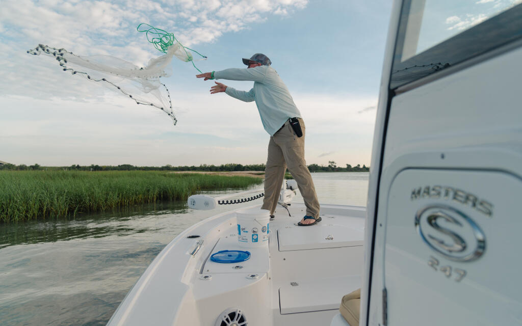 Angler casting a net from the bow of a bay boat in shallow marsh waters