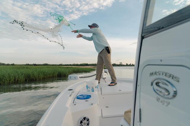 Angler casting a net from the bow of a bay boat in shallow marsh waters