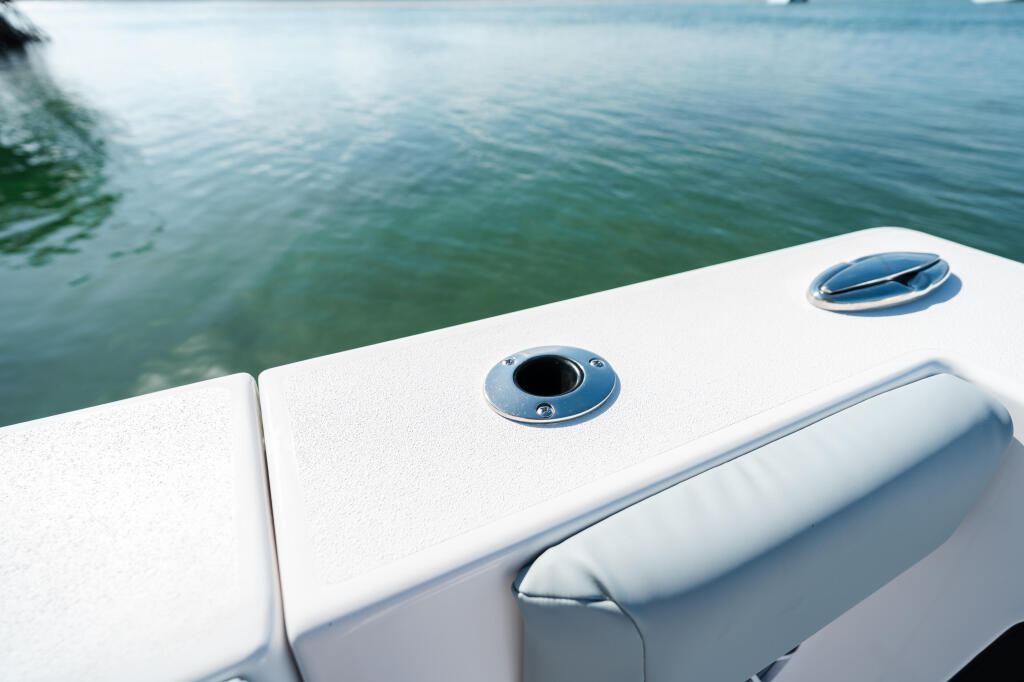 White boat gunwale with stainless steel hardware and ventilation ports overlooking calm green water