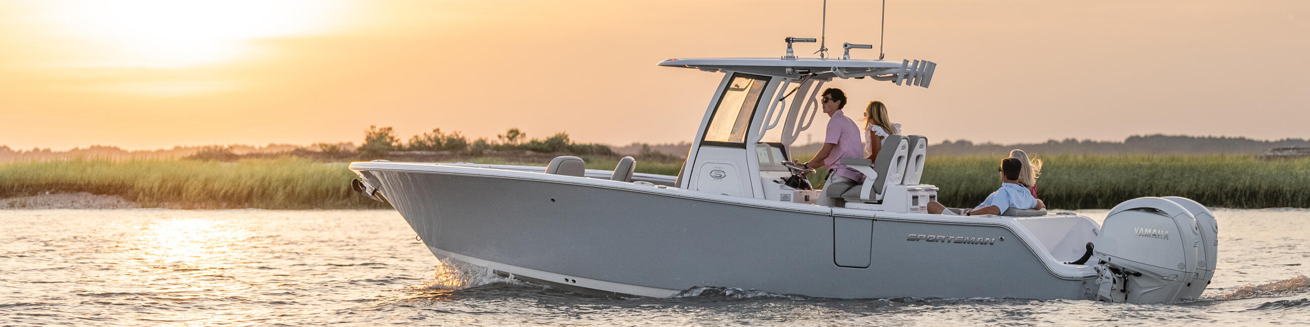 Family and friends cruise in a center console boat at golden hour near salt marsh grass