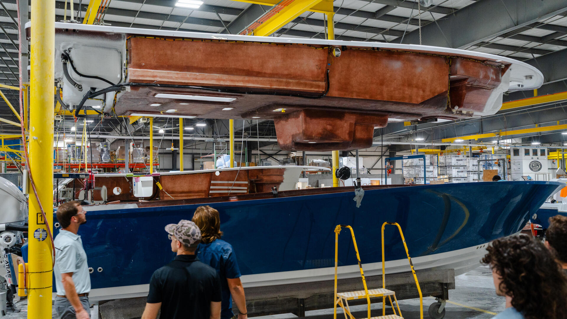 Boat hull under construction in industrial facility with workers examining the wooden interior structure