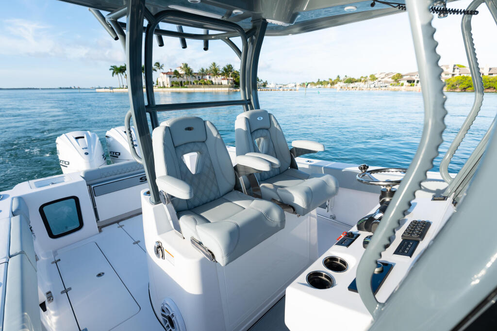 Center console helm with dual captain's chairs and hardtop overlooking calm turquoise water and coastal homes