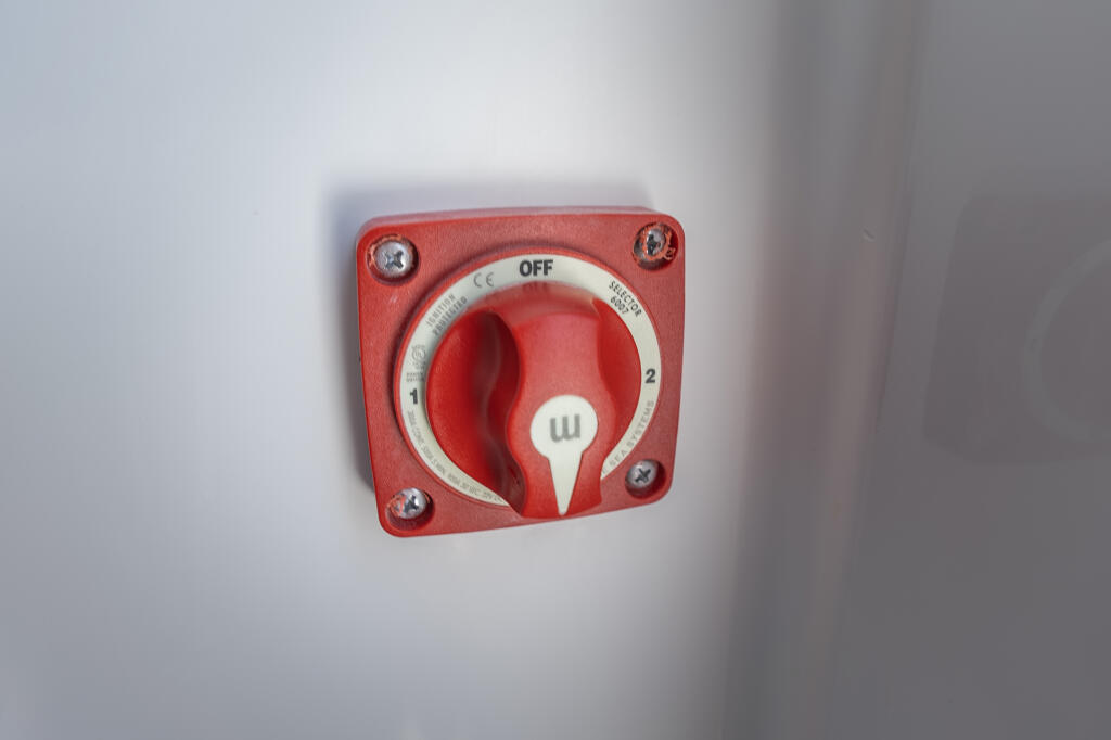 Red marine battery switch with OFF and numbered positions mounted on white panel