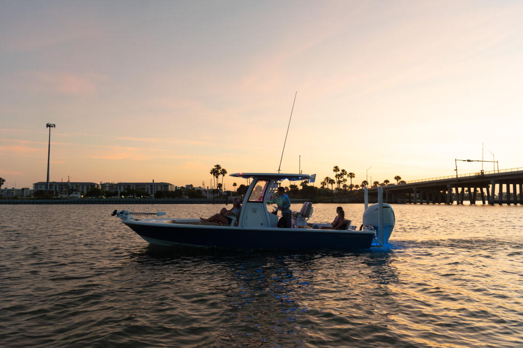 Fishing boat anchored in shallow water at sunset with bridge and palm trees in the distance